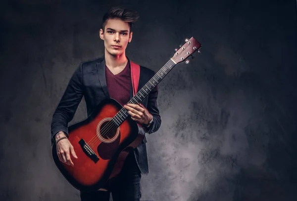 Stijlvolle jonge muzikant met stijlvolle haren in elegante kleding, spelen op een akoestische gitaar. — Stockfoto