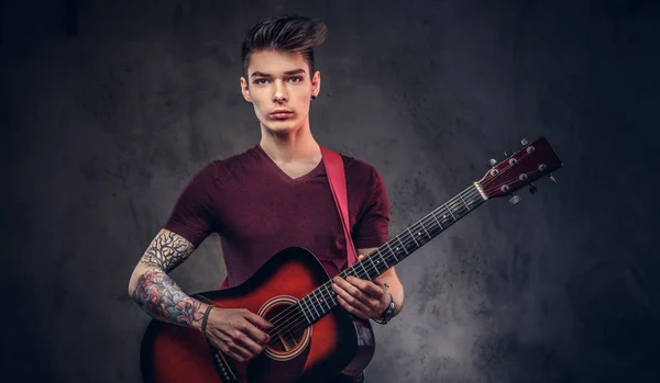 Handsome young musician with stylish hair in a t-shirt, holds a guitar in his hands and playing.