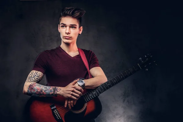 Knappe jonge muzikant met stijlvolle haren in een t-shirt poseren met een gitaar in zijn handen. — Stockfoto