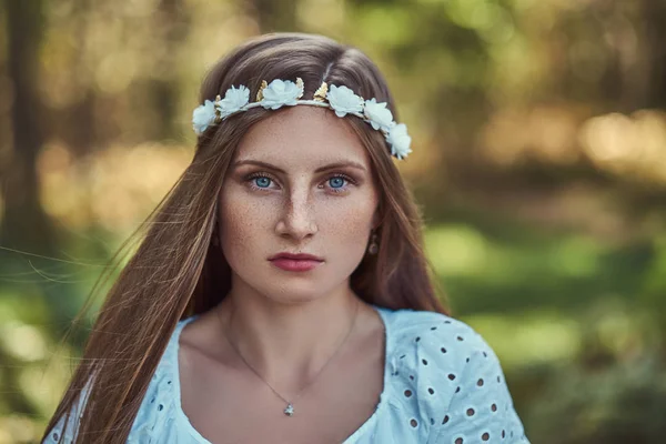Güzel bir kadın beyaz elbise ve beyaz çelenk kafa yeşil bir sonbahar ormanda poz üzerinde.