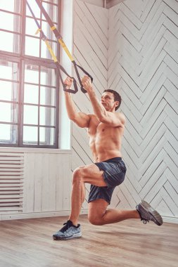 Trx ile egzersiz yaparak gömleksiz kaslı erkek.