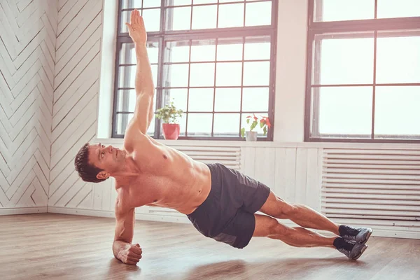 Hombre musculoso guapo sin camisa haciendo ejercicios funcionales en el suelo en casa . —  Fotos de Stock