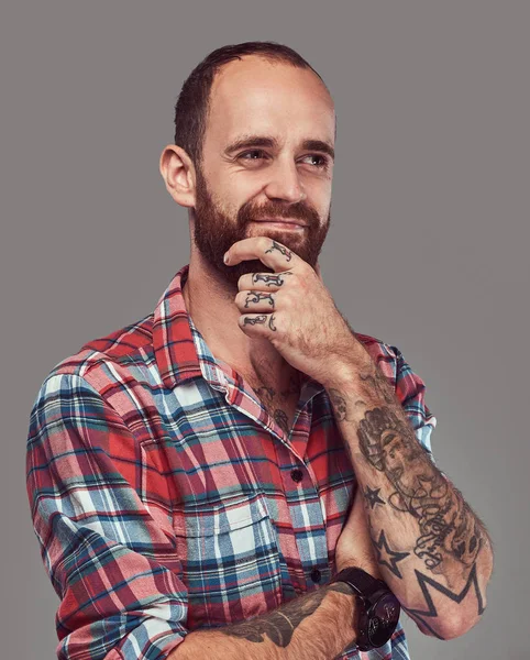 Retrato de un guapo hipster elegante tatuado con una barba bien recortada en una camisa de franela, posando en un estudio . — Foto de Stock