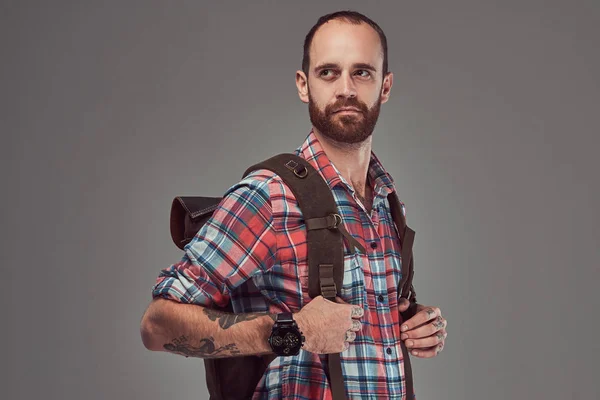 Retrato de um belo viajante tatuado em uma camisa de flanela com uma mochila, de pé em um estúdio . — Fotografia de Stock