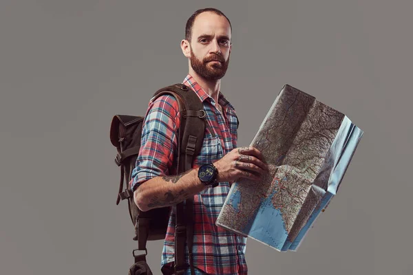 Portrét pohledný Tetovaný cestovatel v flanelovou košili s batohem, obsahuje mapu, stojící ve studiu. — Stock fotografie