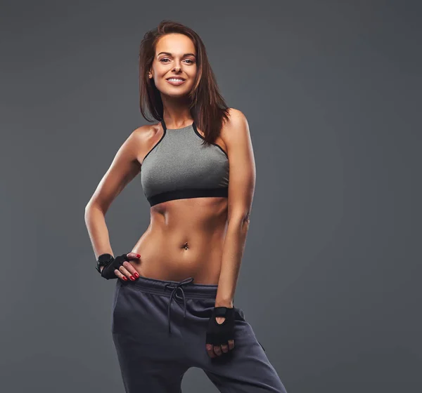 Uśmiechnięta brunetka dama fitness w szary sportowej pozowanie w studio. — Zdjęcie stockowe