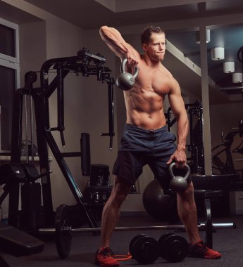 Yakışıklı kaslı gömleksiz vücut geliştirmeci erkek spor salonunda bir dumbbell ile yapıyor.