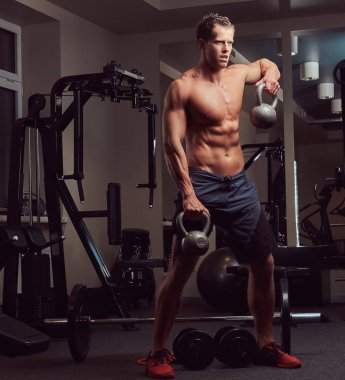 Yakışıklı kaslı gömleksiz vücut geliştirmeci erkek spor salonunda bir dumbbell ile yapıyor.