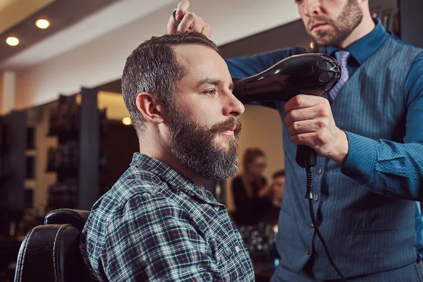 Barbier professionnel travaillant avec un client dans un salon de coiffure, utilise un sèche-cheveux . — Photo