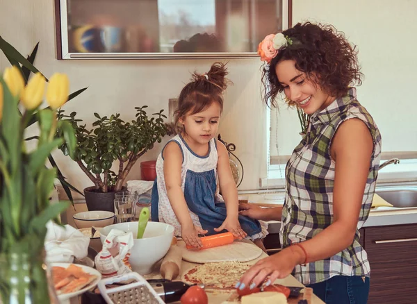 Schöne hispanische Mutter lehrt ihre süße kleine Tochter Pizza zubereiten in der Küche. — Stockfoto