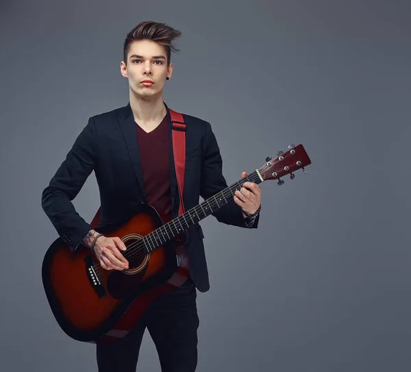 Handsome young musician with stylish hair in elegant clothes, playing on an acoustic guitar. — Stock Photo, Image