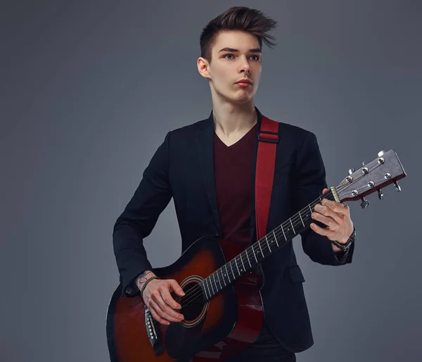 Knappe jonge muzikant met stijlvolle haren in elegante kleding, spelen op een akoestische gitaar. — Stockfoto