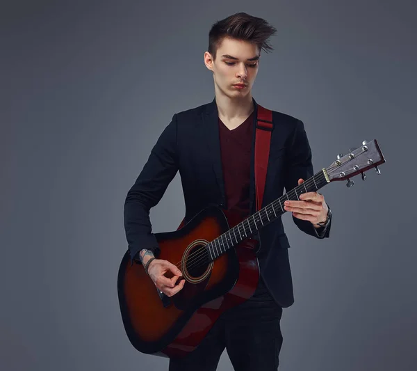 Guapo joven músico con el pelo elegante en ropa elegante, tocando en una guitarra acústica . — Foto de Stock