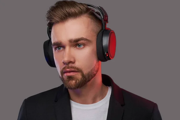 Close-up portrait of a stylish bearded man with hairstyle listening to music in headphones. — Stock Photo, Image