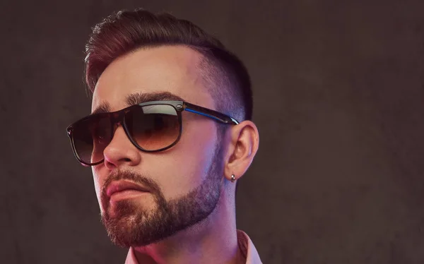 Nahaufnahme Porträt eines selbstbewussten bärtigen Mannes mit Frisur und Sonnenbrille im grauen Anzug und rosa Hemd, der in einem Studio posiert. — Stockfoto