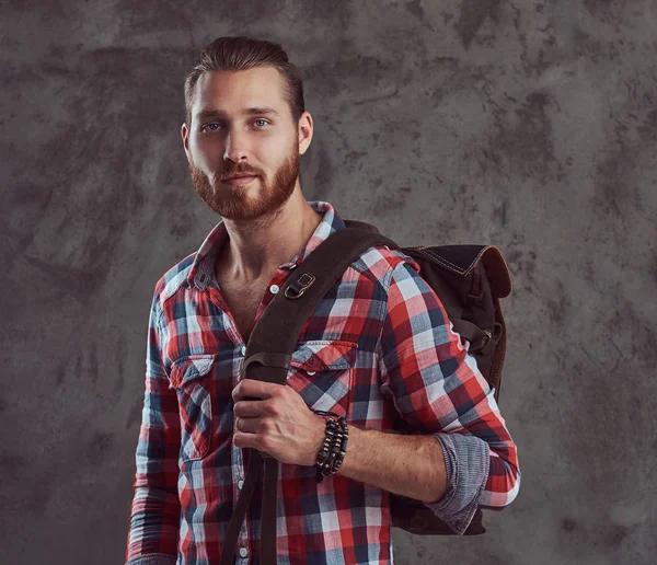 Bonito viajante ruiva elegante em uma camisa de flanela com uma mochila, posando em um estúdio em um fundo cinza . — Fotografia de Stock