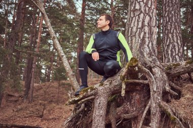 Jogger ormandaki bir ağaç altında oturur ve uzak, uzun vadede sonra dinlenme görünüyor. Aktif bir şekilde yaşam.