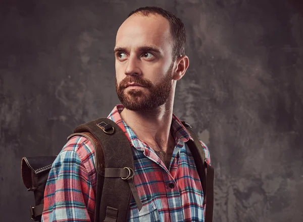 Retrato de um belo viajante tatuado em uma camisa de flanela com uma mochila, de pé em um estúdio . — Fotografia de Stock