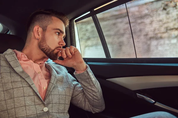 成功时尚的年轻商人穿着灰色西装和粉红色的衬衫, 骑在后座豪华轿车. — 图库照片