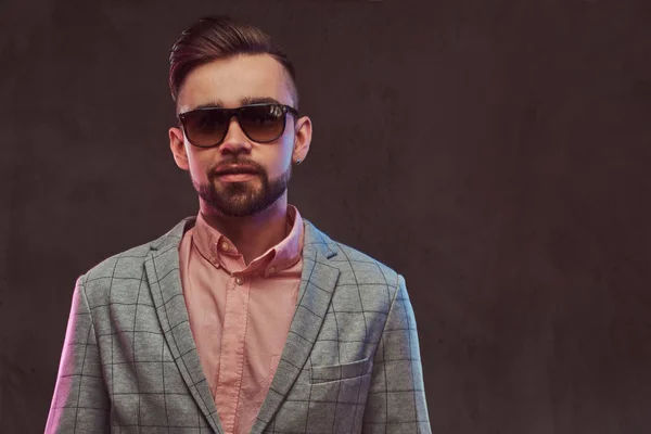 Retrato de cerca de un hombre barbudo con estilo y confianza con peinado y gafas de sol en un traje gris y camisa rosa, posando en un estudio . — Foto de Stock