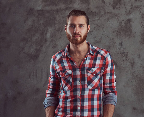 Young handsome redhead model man in a flannel shirt on a gray background.