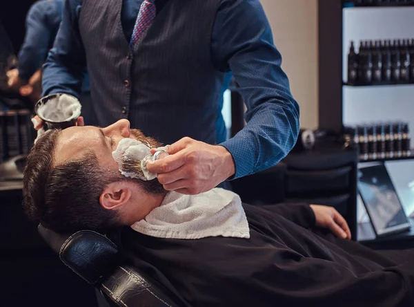 Peluquería Maestro prepara la cara para el afeitado y unta la cara con espuma en un salón de peluquería . —  Fotos de Stock