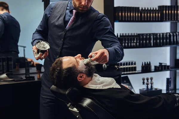Мастер парикмахер готовит лицо к бритью и мажет лицо пеной в парикмахерской . — стоковое фото