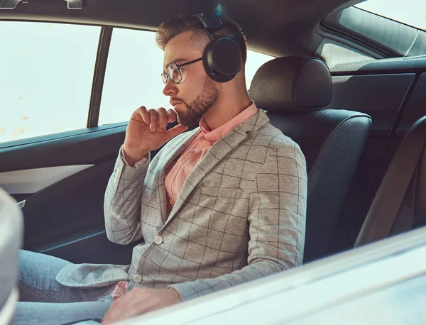Joven empresario con estilo de éxito en un traje gris y camisa rosa, montado en un asiento trasero en un coche de lujo . — Foto de Stock
