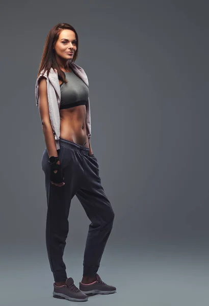 Slim fitness brunette femme dans un vêtement de sport gris posant dans un studio . — Photo