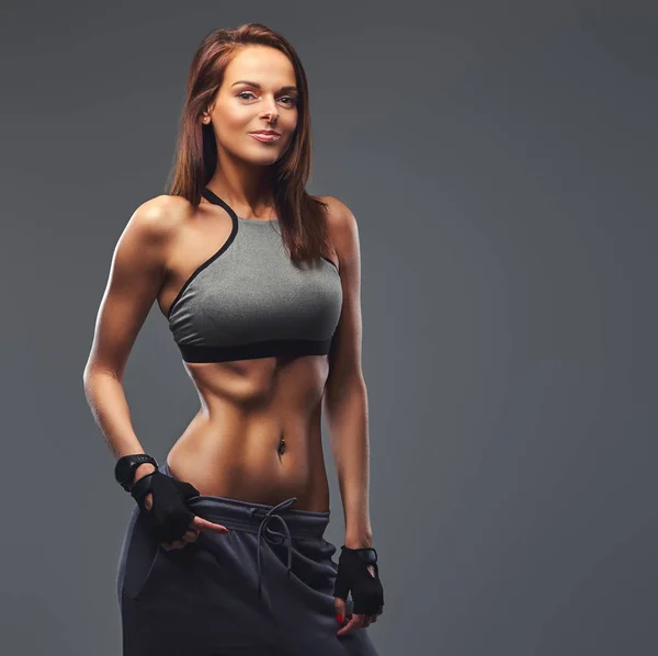 Schlanke Fitness brünette Frau in grauer Sportbekleidung posiert in einem Studio. — Stockfoto