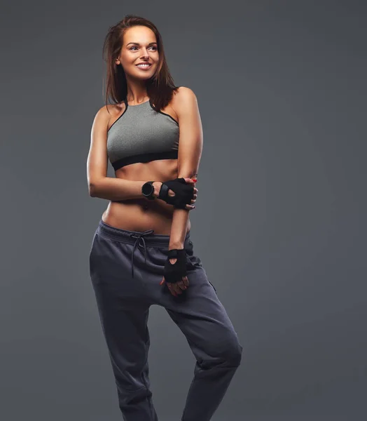 Sorrindo fitness mulher morena em um sportswear cinza posando em um estúdio . — Fotografia de Stock