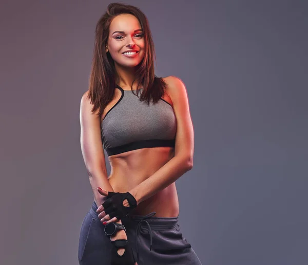 Sonriente morena fitness mujer en una ropa deportiva gris posando en un estudio . —  Fotos de Stock