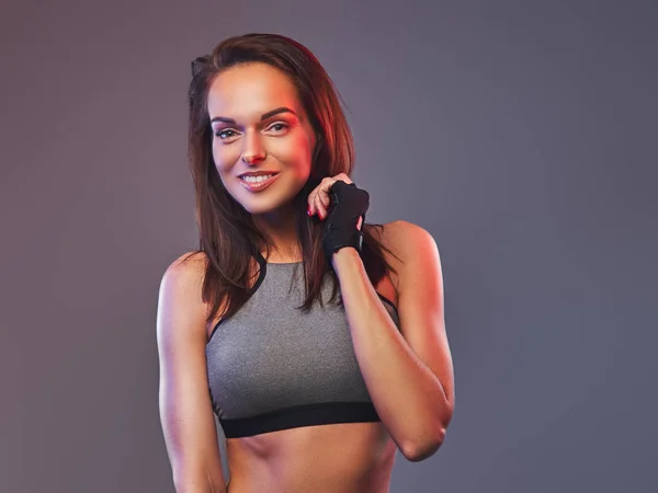 Lachende fitness brunette vrouw in een grijze sportkleding poseren in een studio. — Stockfoto