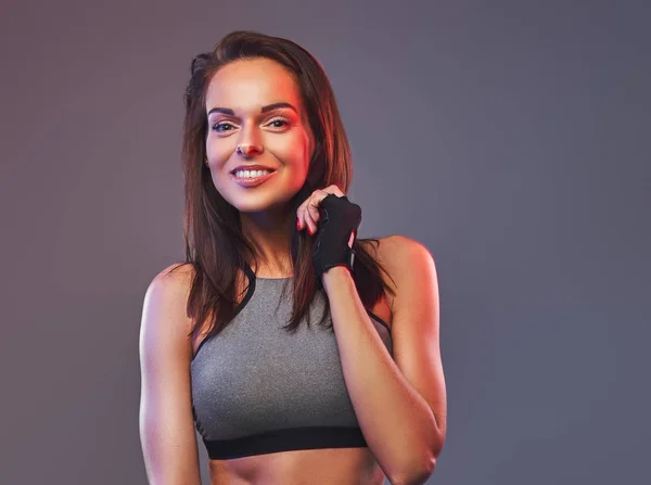Lächelnde Fitness-Brünette in grauer Sportbekleidung posiert in einem Studio. — Stockfoto