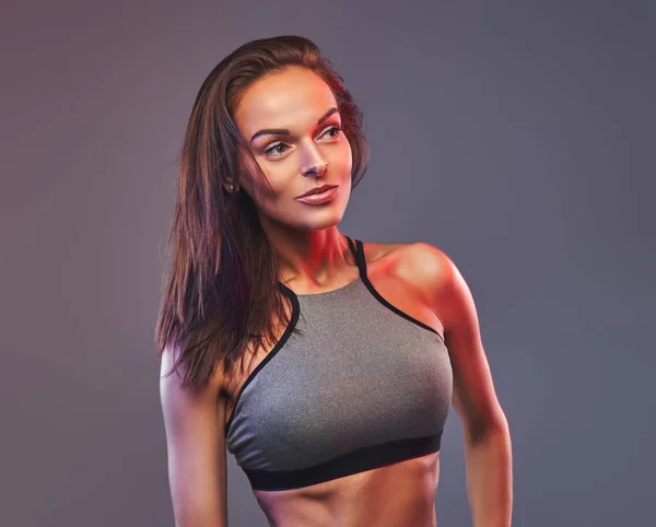 Schlanke Fitness brünette Frau in grauer Sportbekleidung posiert in einem Studio. — Stockfoto