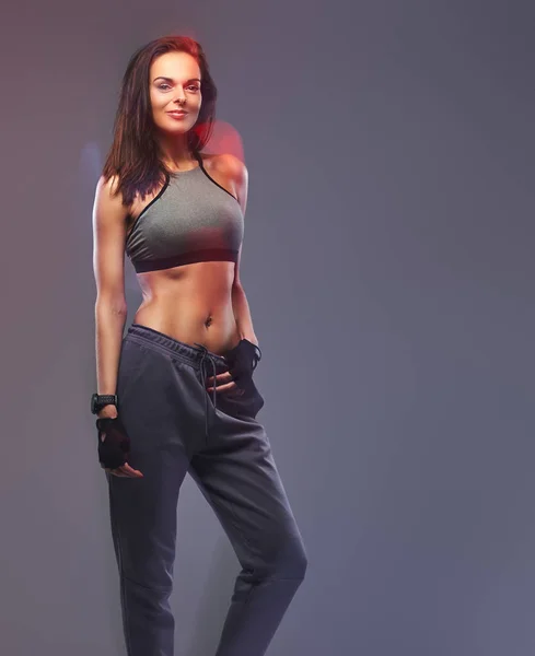 Slim fitness brunette vrouw in een grijze sportkleding poseren in een studio. — Stockfoto