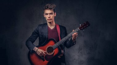 Bir akustik gitar çalmaya şık giysiler içinde şık saç ile şık genç müzisyen.