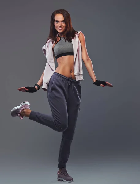 Smiling fitness brunette woman in a gray sportswear posing in a studio. — Stock Photo, Image