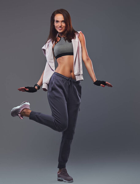 Smiling fitness brunette woman in a gray sportswear posing in a studio.