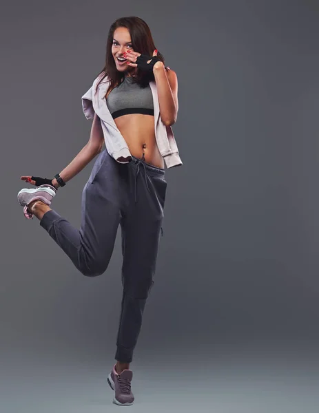 Sorridente donna bruna fitness in un abbigliamento sportivo grigio in posa in uno studio . — Foto Stock