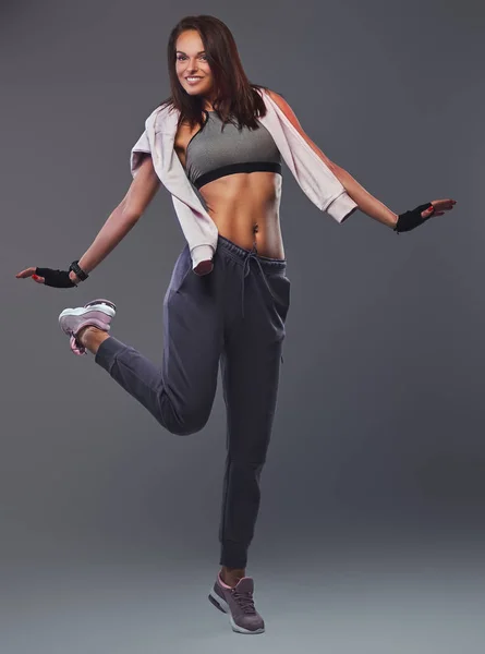 Smiling fitness brunette woman in a gray sportswear posing in a studio. — Stock Photo, Image