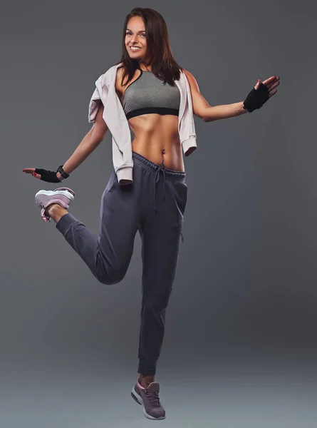 Leende fitness brunett kvinna i en grå sportkläder som poserar i en studio. — Stockfoto
