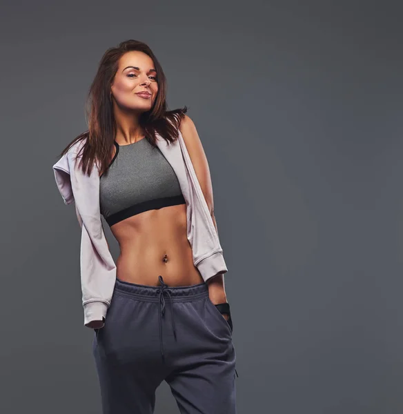 Sorridente donna bruna fitness in un abbigliamento sportivo grigio in posa in uno studio . — Foto Stock