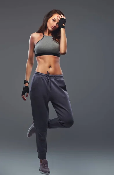 Slim fitness donna bruna in uno sportswear grigio in posa in uno studio . — Foto Stock