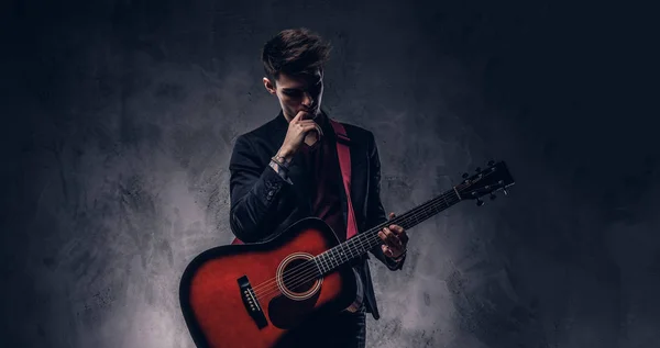 Yakışıklı genç düşünceli müzisyen şık giysileriyle onun elinde bir gitar ile poz şık saç ile. — Stok fotoğraf