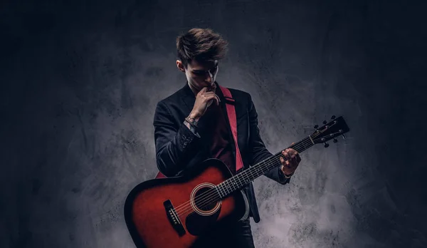 Knappe jonge doordachte musicus met stijlvolle haren in elegante kleding poseren met een gitaar in zijn handen. — Stockfoto