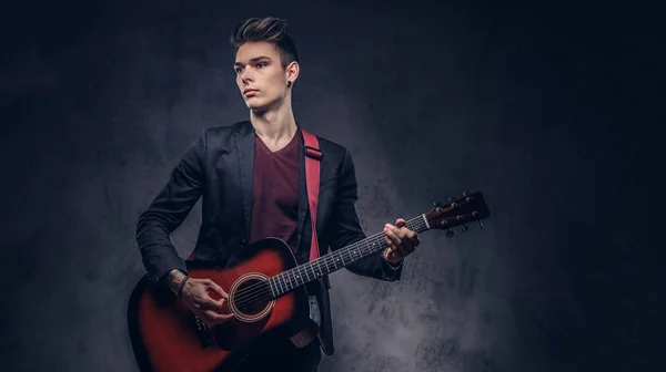 Κομψό νεαρός μουσικός με κομψά μαλλιά με κομψά ρούχα, παίζοντας σε μια ακουστική κιθάρα. — Φωτογραφία Αρχείου