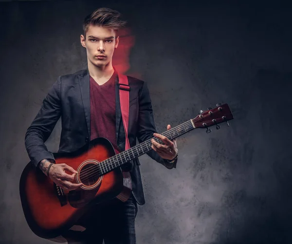 Jeune musicien élégant avec des cheveux élégants dans des vêtements élégants, jouant sur une guitare acoustique . — Photo
