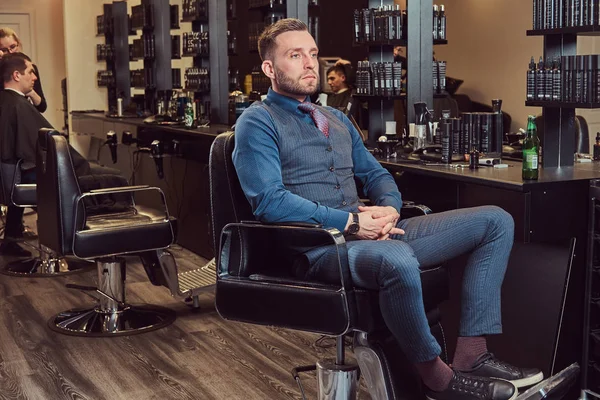 Ein professioneller Friseur sitzt auf einem Sessel und ruht sich nach der Arbeit mit einer Bierflasche in der Hand aus. — Stockfoto