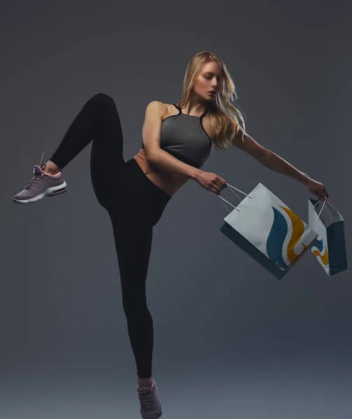 Vacker blond flicka lyfter benet med paket i händerna. — Stockfoto